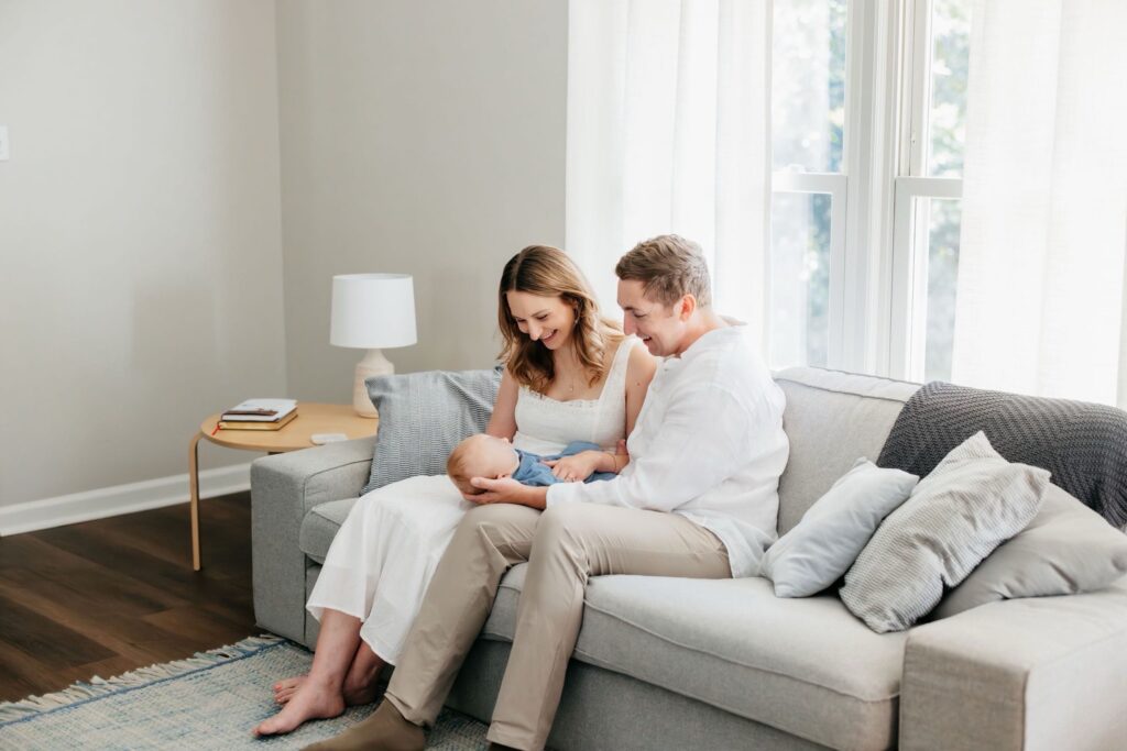Mom and dad sitting on a couch staring at their baby in their arms.